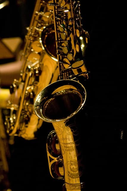 detail zlatého saxofonu položeného ve stojanu, tmavé pozadí